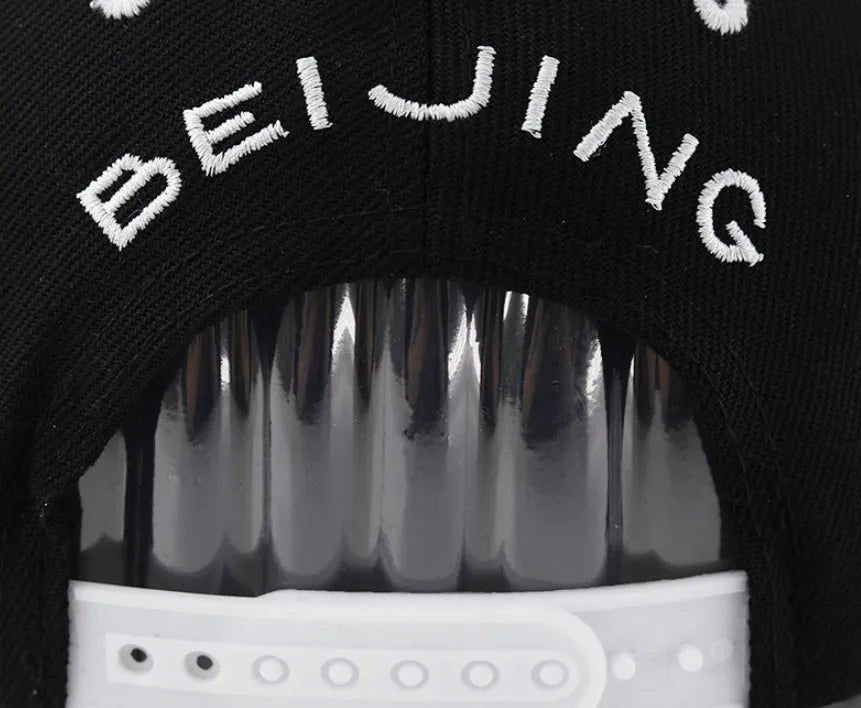 Cotton baseball cap with embroidered letters in black or white, showing adjustable strap.